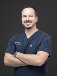 Picture of a male dentist standing upright and smiling with his arms crossed.